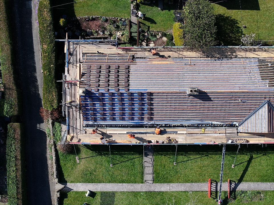 Aerial view of solar panel installation in progress on residential rooftop with workers visible from above.