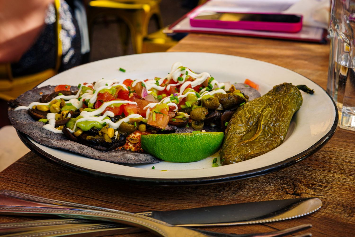 Mexican tostada with black beans, avocado, tomato, lime, and sour cream on a dark tortilla.