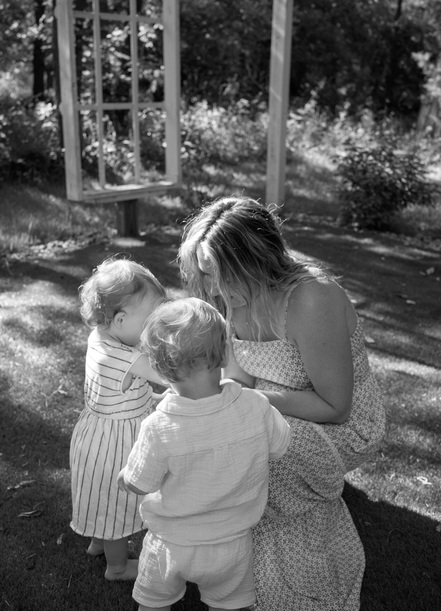 Black and white photo showing tender family moments in a wooded outdoor setting.