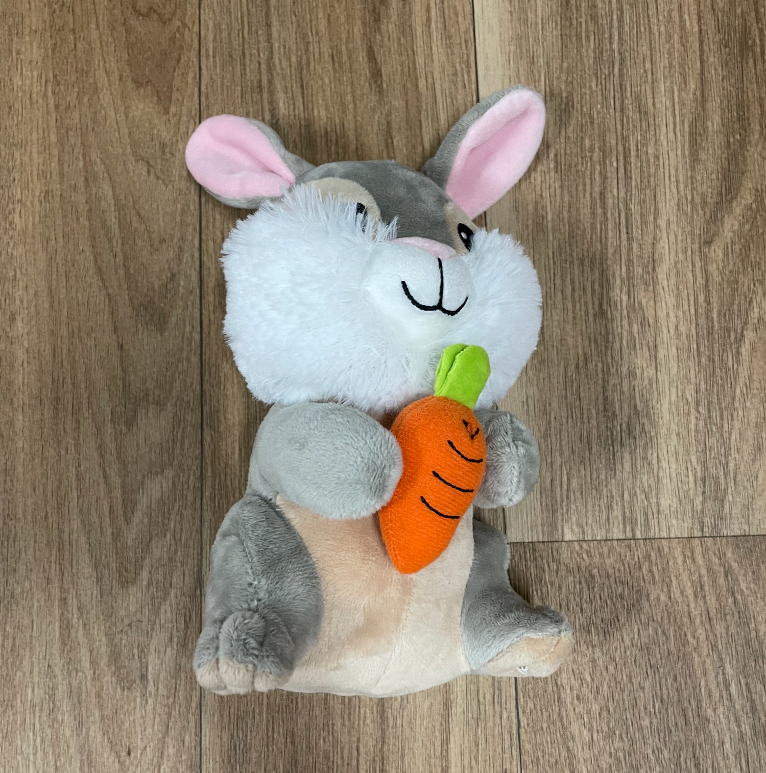 Cute bunny plush toys with orange carrots lying on wooden flooring.
