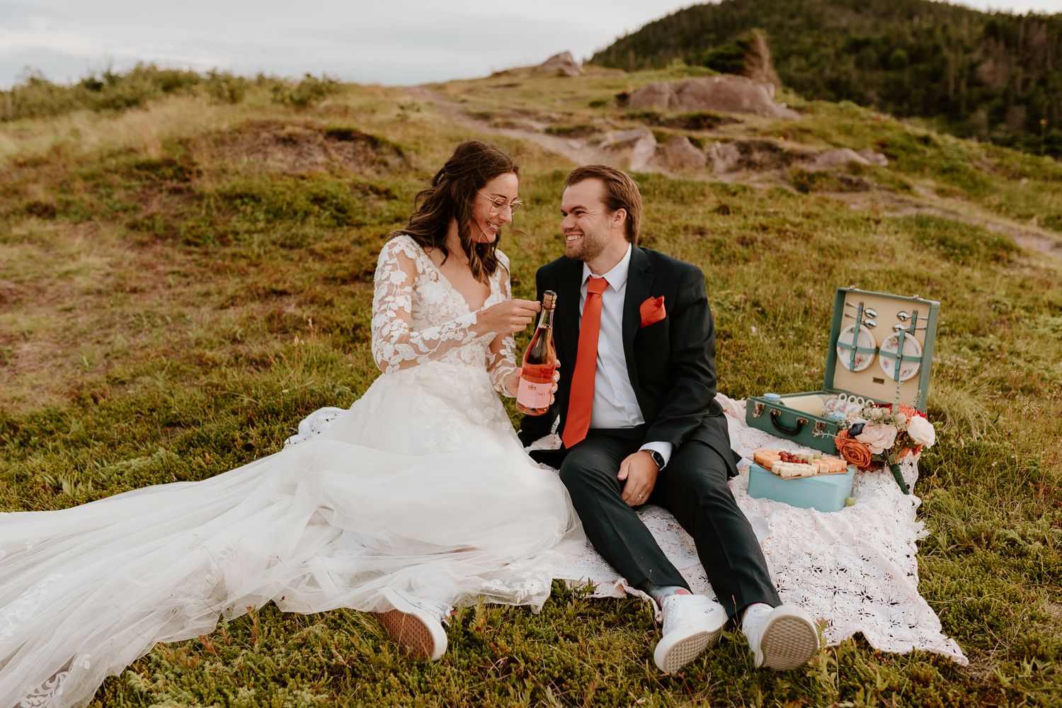 bride and groom at a picnic pouring each other champagne from a bottle