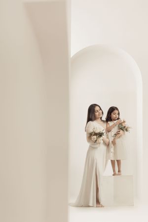 Artistic family portrait with white dresses and floral bouquets in minimalist archway setting.