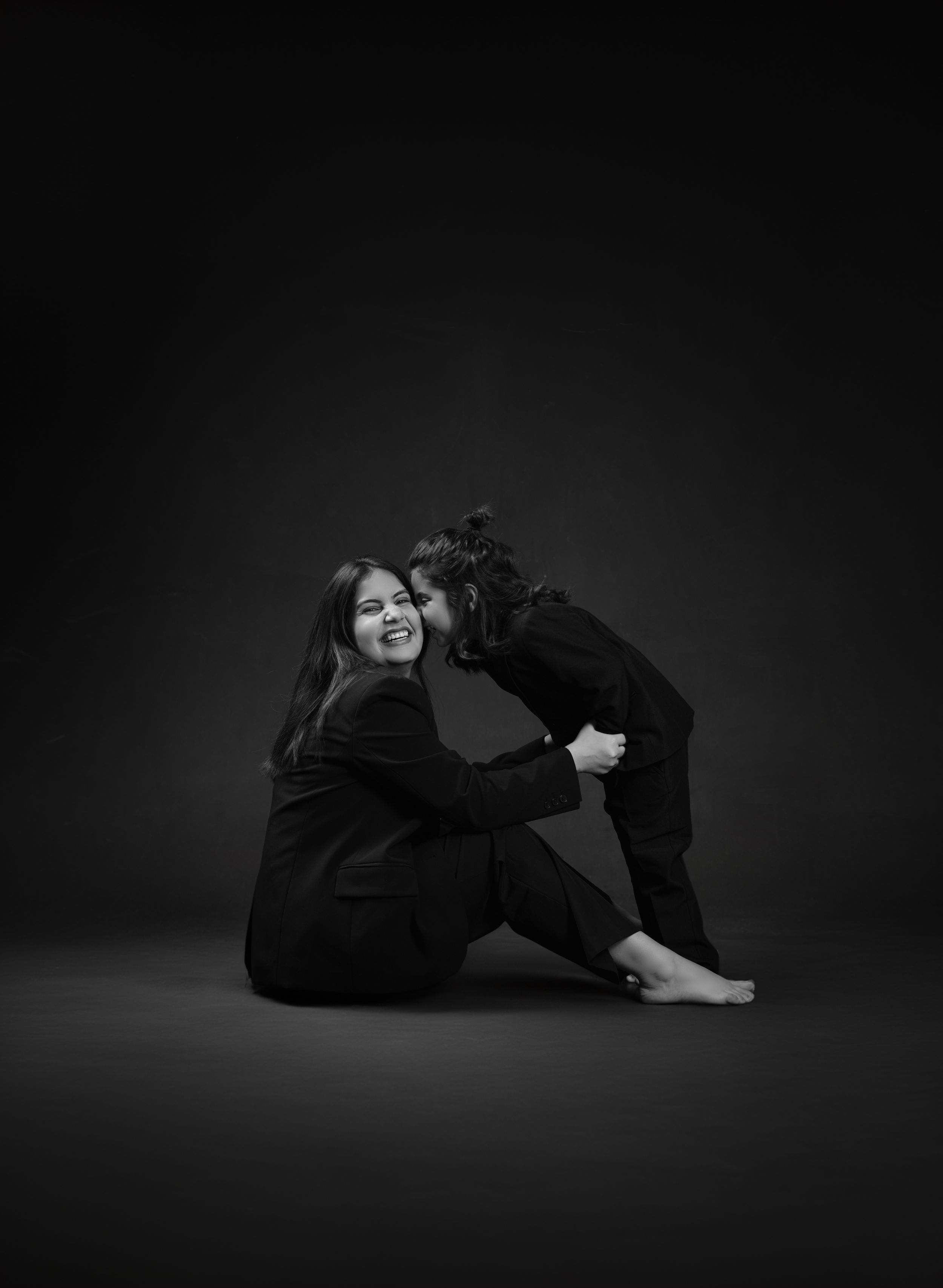 Intimate black and white portrait of two people embracing on dark background.