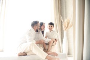 Bright and airy indoor family moment captured on white bedding near window.
