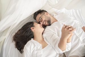 Couple sharing an intimate moment while lying on white bedding.