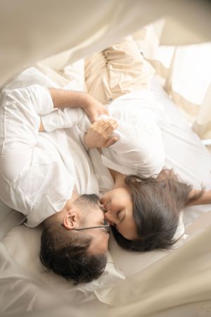 Couple lying together on white bedding in soft natural light.