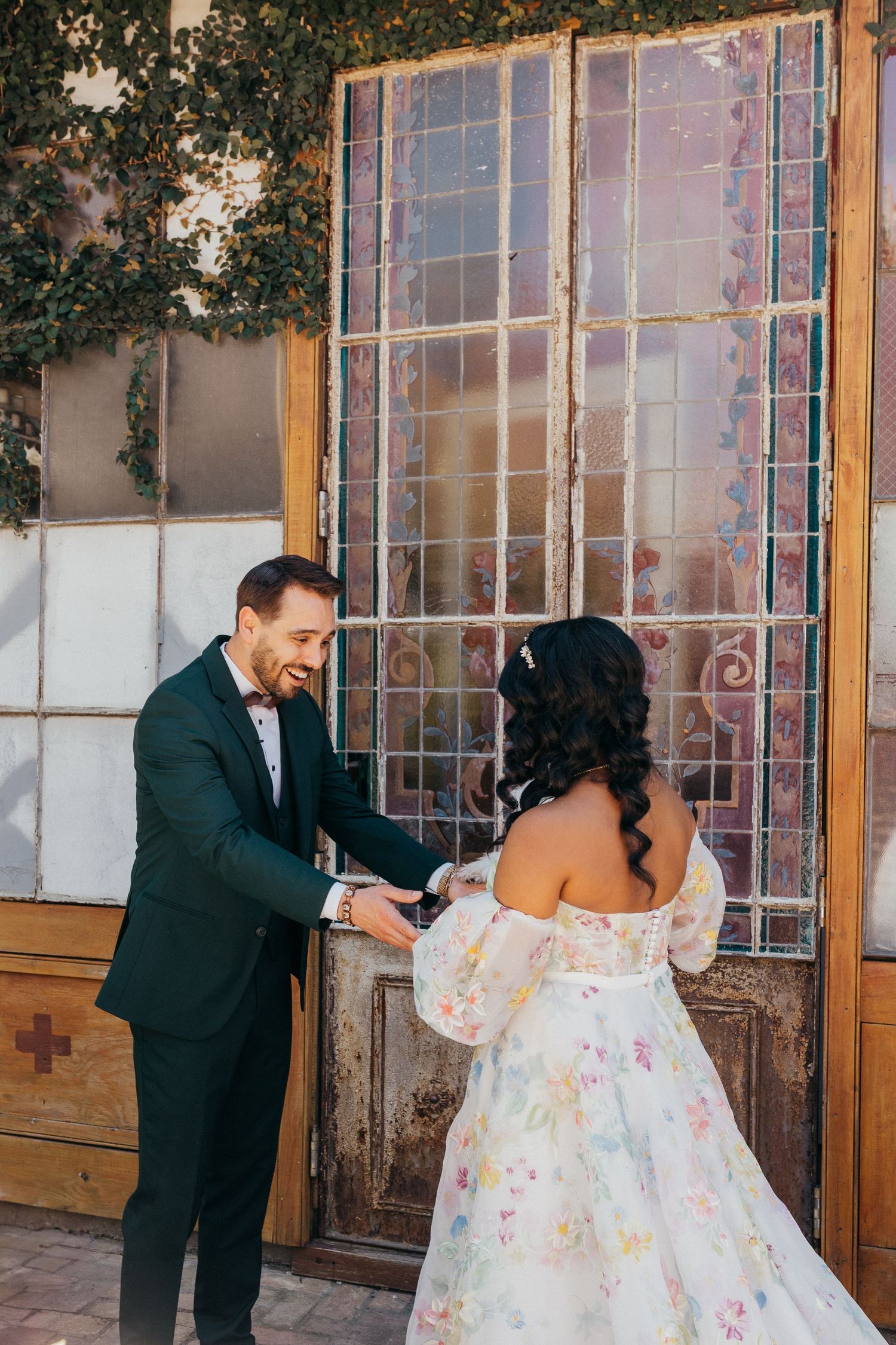 A wedding couple shares romantic kisses along a bright sunny wall in a rustic alley adorned with palm trees.