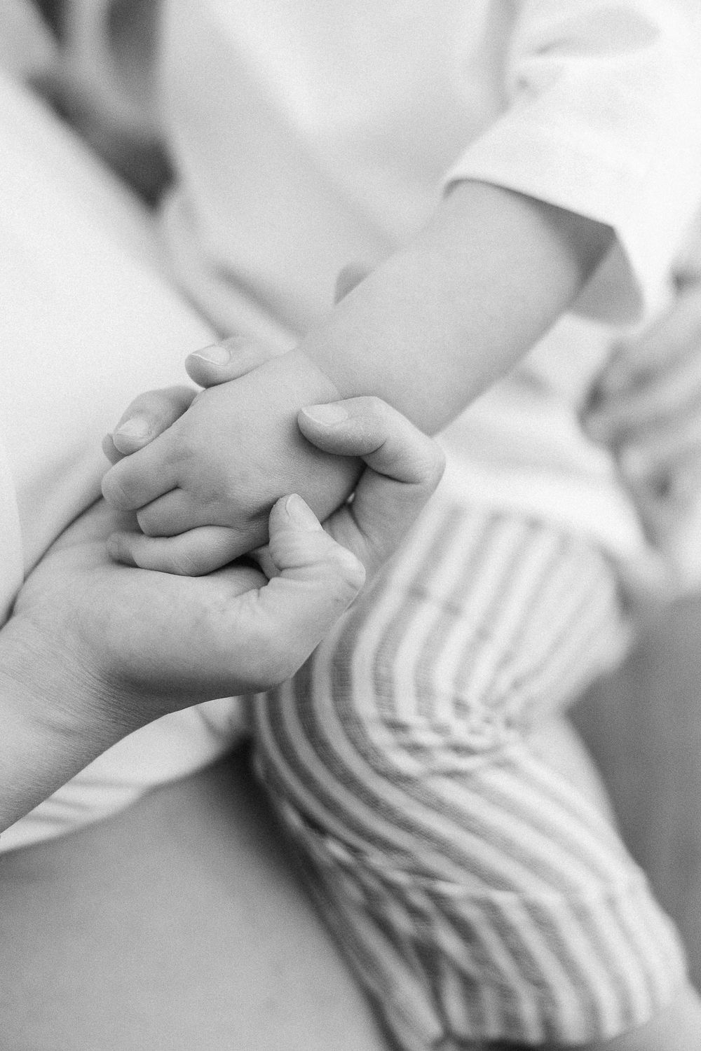 A close-up black and white photo of hands holding each other in a tender gesture.