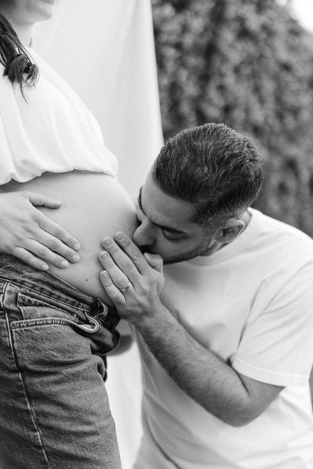 Black and white maternity photo showing someone kissing a pregnant belly while wearing a white t-shirt.