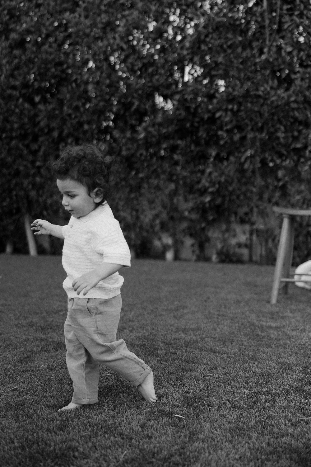 Black and white photograph of small child playing in a grassy backyard, wearing casual clothing.