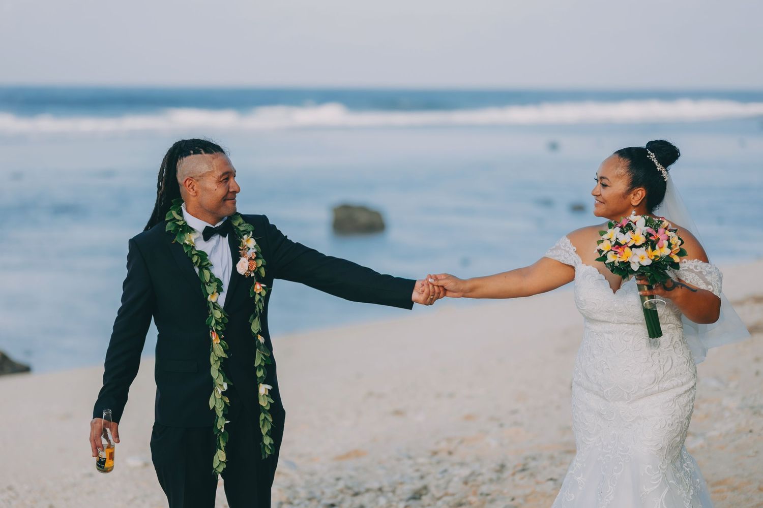 A romantic wedding couple stands on a cliff overlooking a dramatic stormy ocean at sunset.