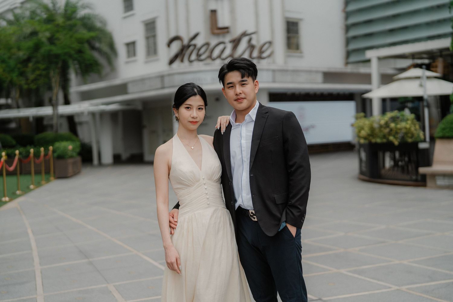 A couple in formal attire stands outside a historic theater building with palm trees in the background.