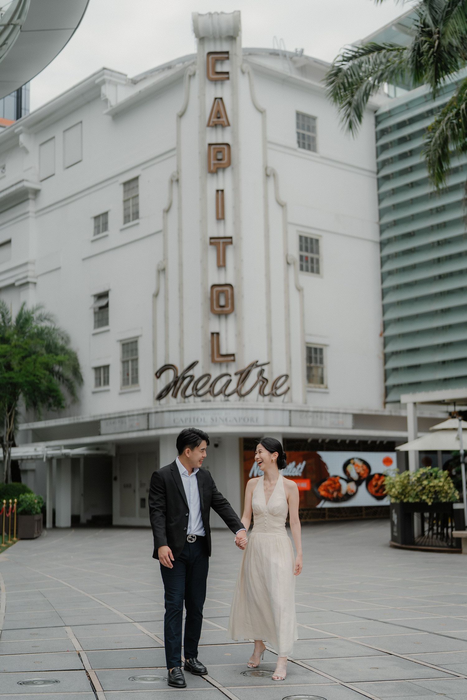 A couple takes a romantic stroll in front of the historic white Capitol Theatre building.