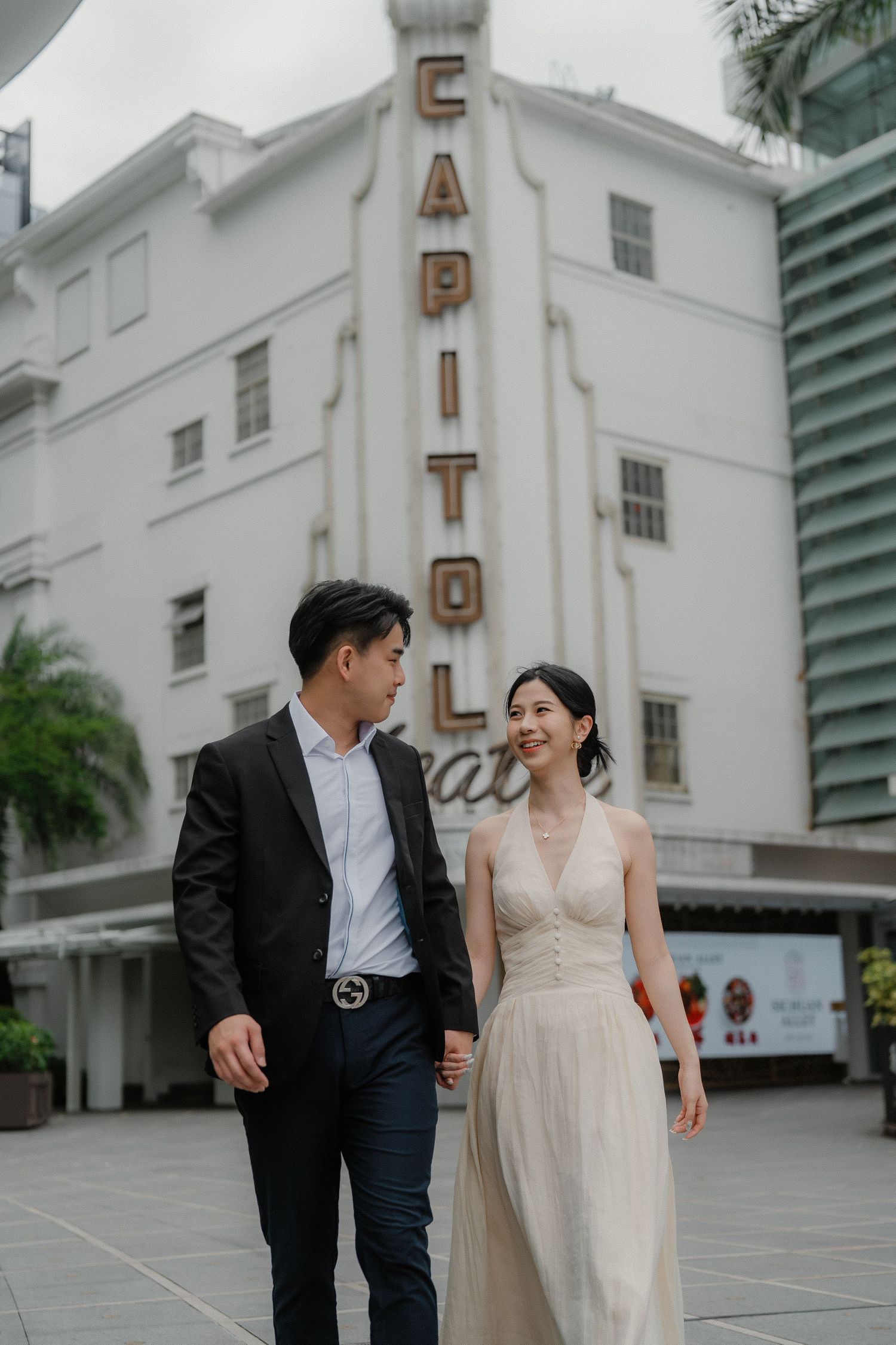 Couple in formal attire strolling together in front of the iconic Capitol Theatre building in Singapore.