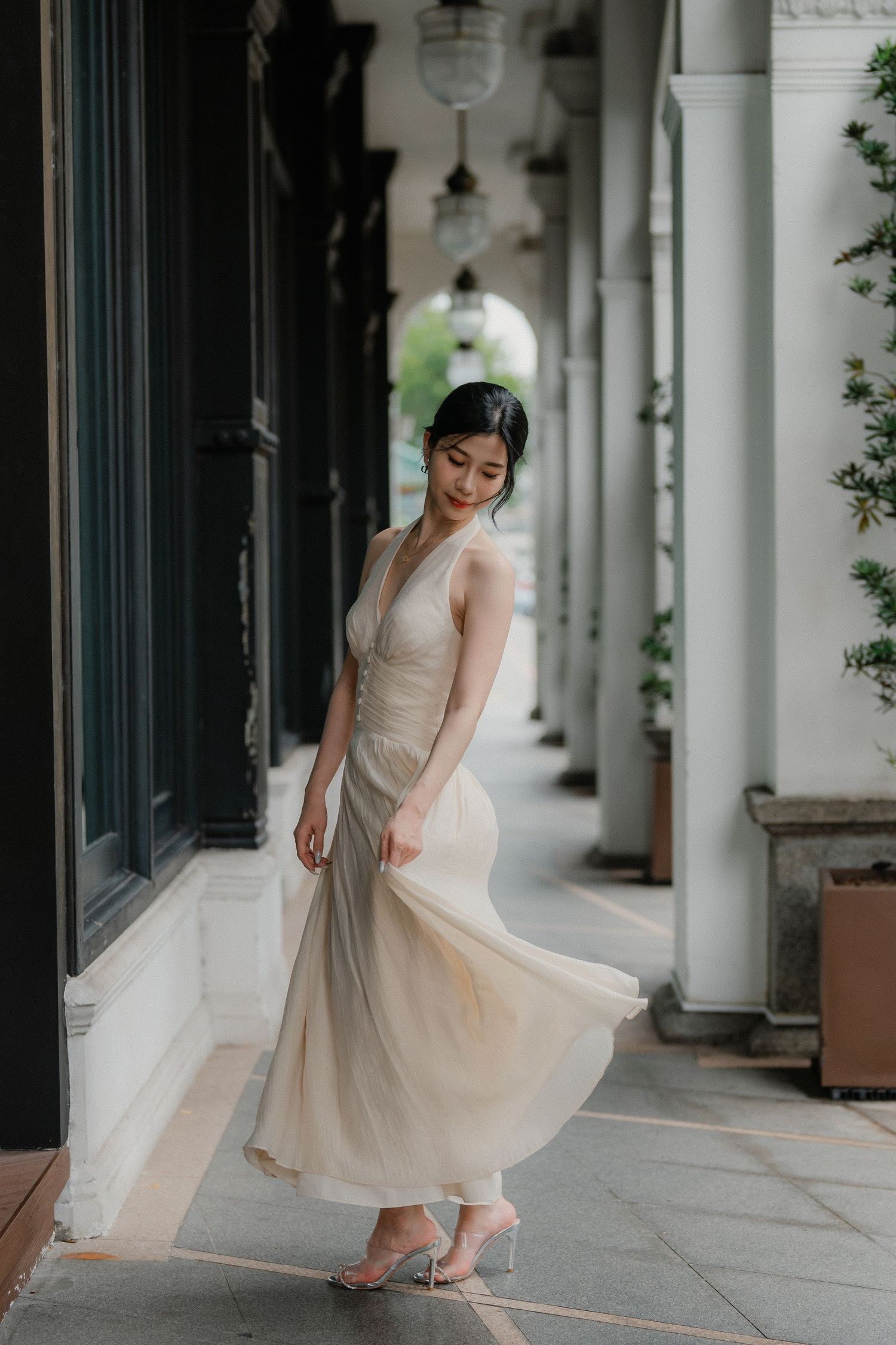 A person in a flowing cream dress twirls in an elegant colonnade hallway with white pillars.