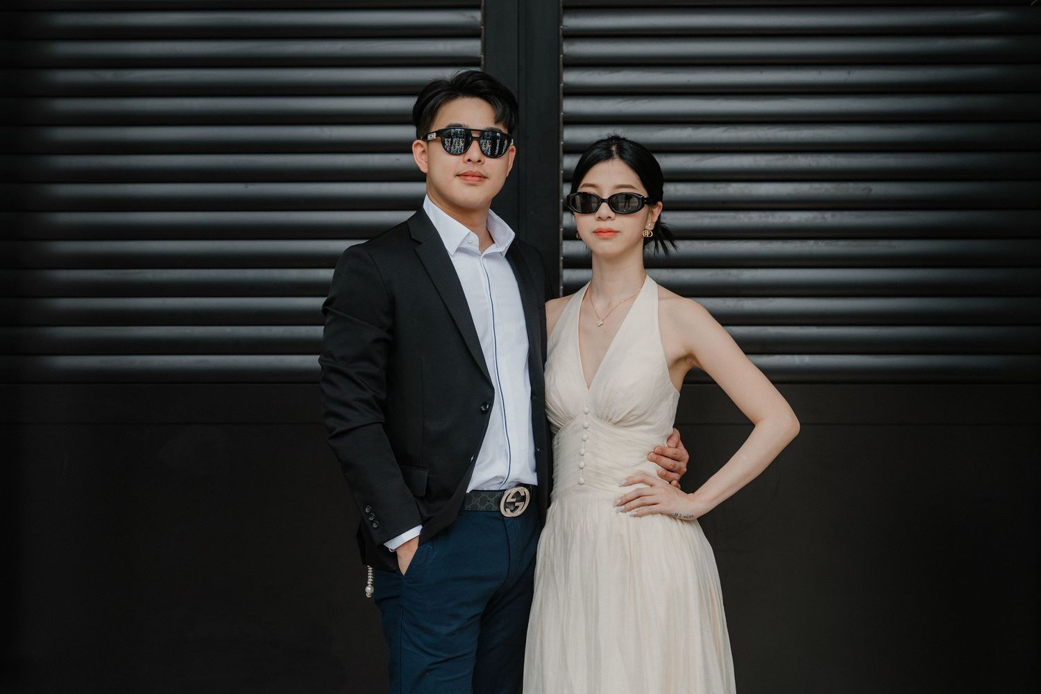 A couple in formal wedding attire poses against a dark industrial backdrop with metal doors.