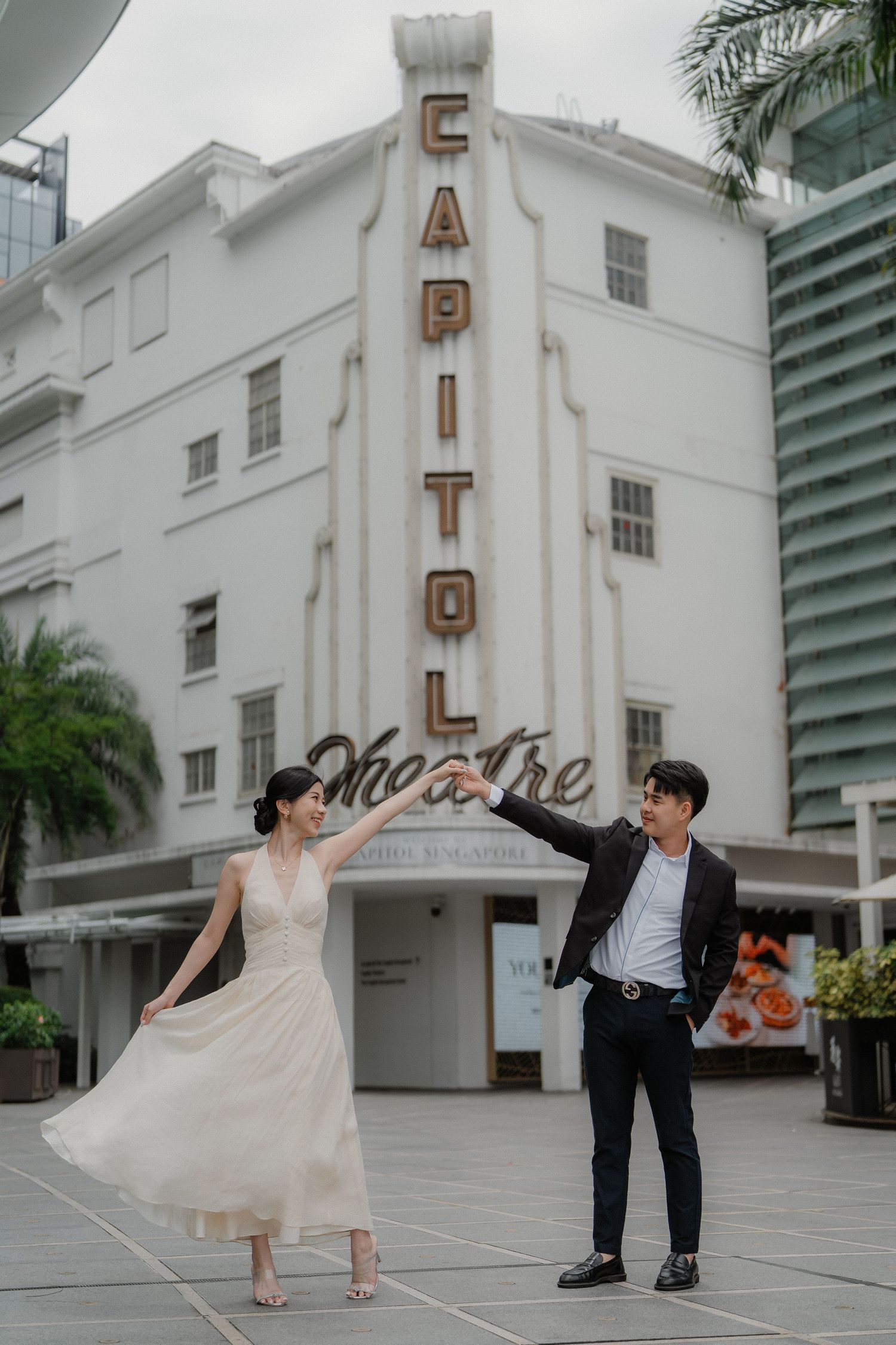 A couple poses in formal attire in front of the iconic white Art Deco Capitol Theatre building in Singapore.