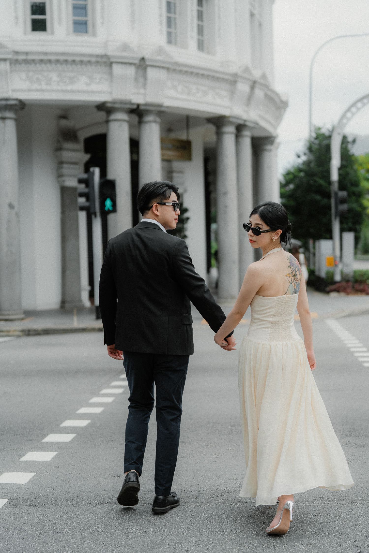 A couple walks along a city street holding hands with classic architecture in the background.