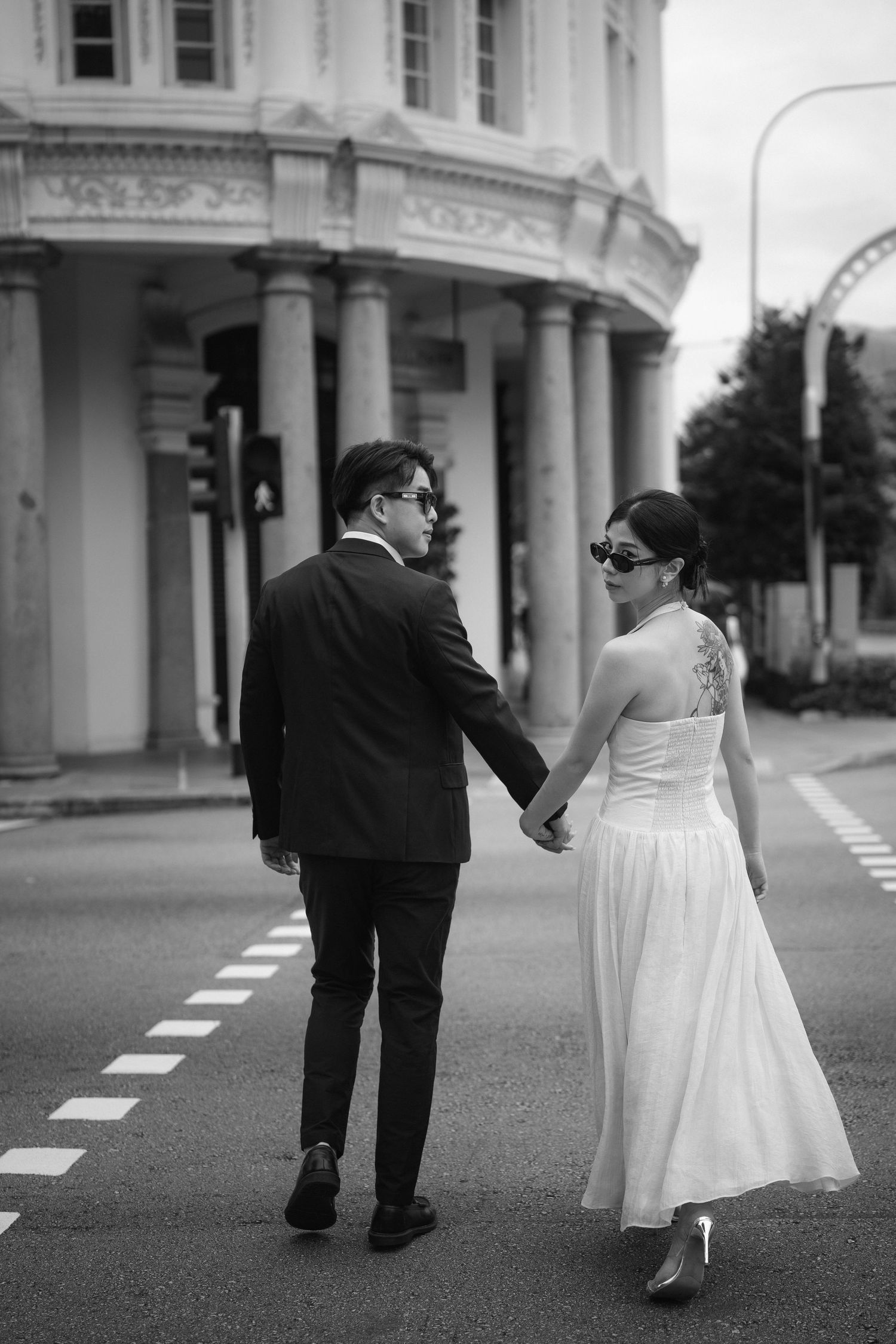 Black and white photo of couple in formal wear walking along street holding hands.