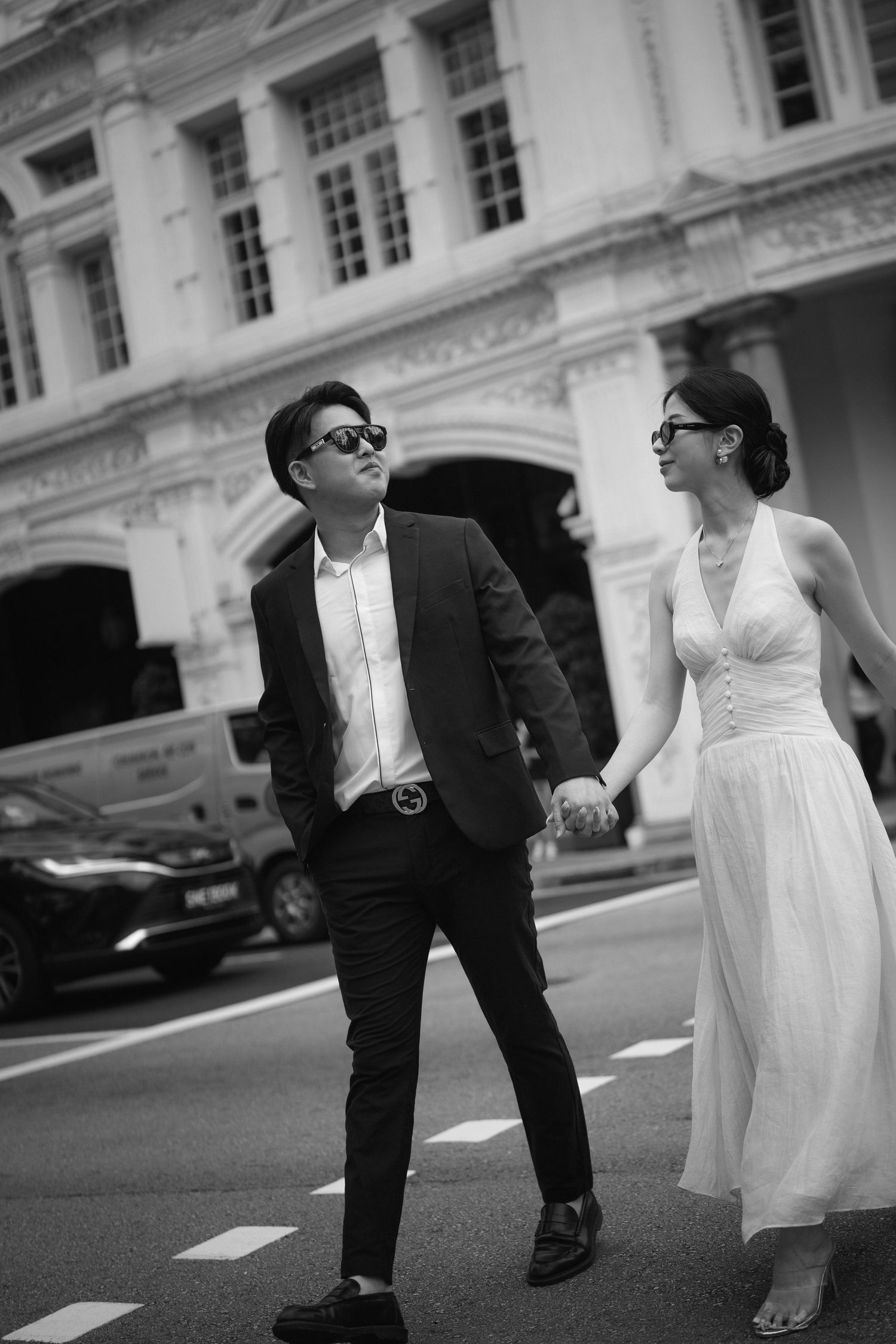 Black and white photo of couple walking in formal attire against classic architectural backdrop.