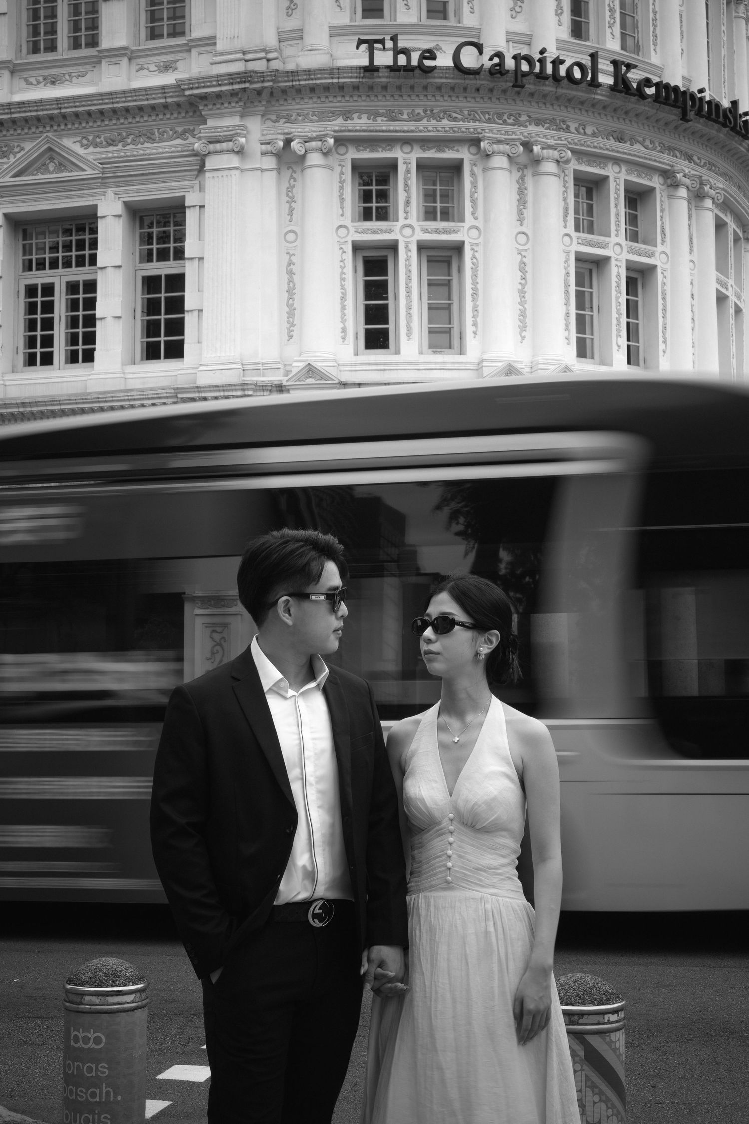 A black and white portrait of a couple with a motion-blurred bus passing behind them.