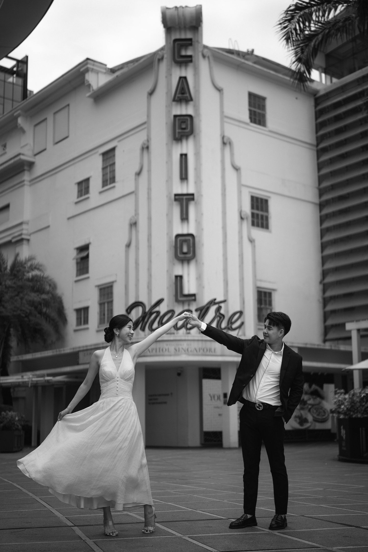 A couple dances in vintage attire outside the art deco Capitol Theatre in black and white photography.