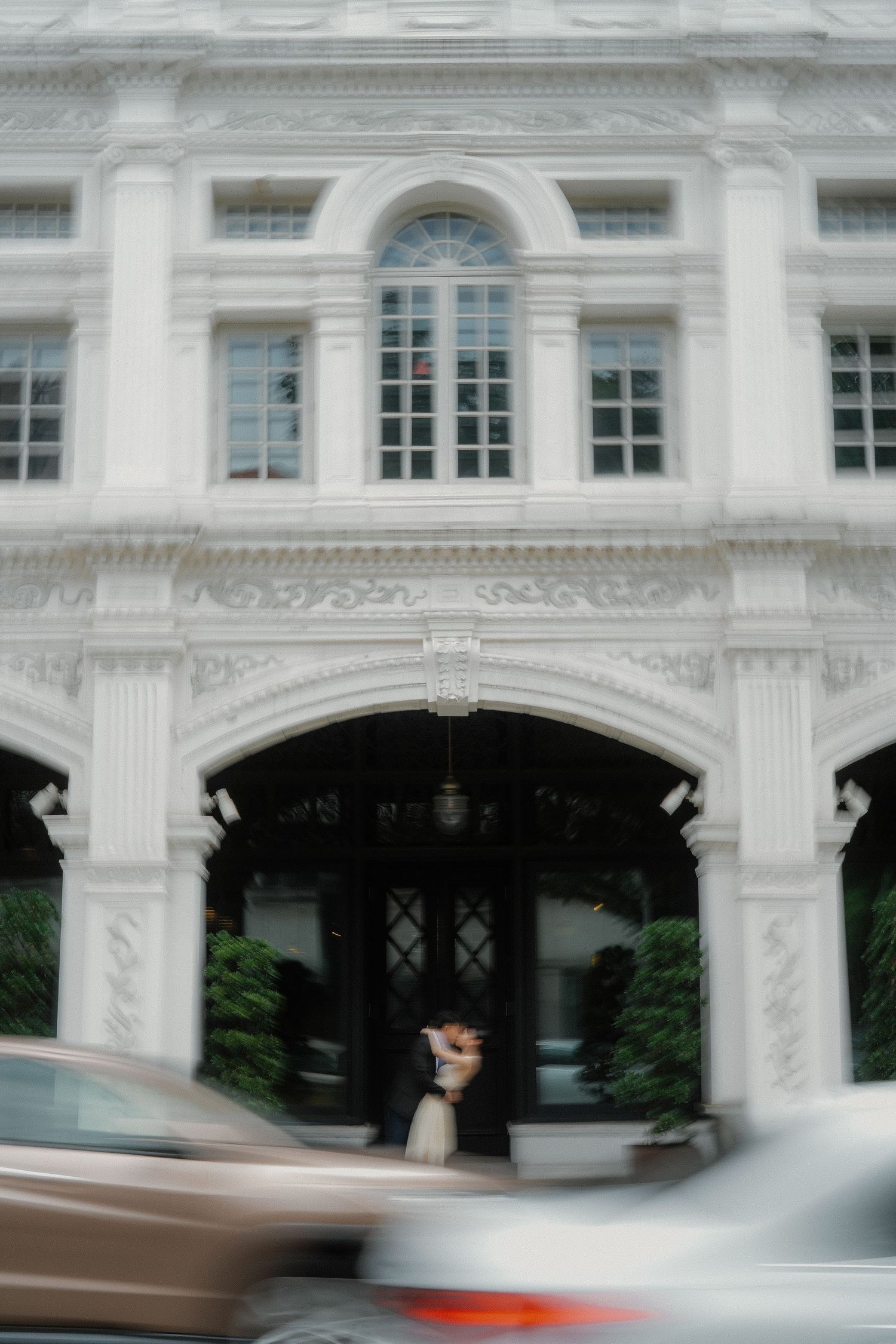 A blurred motion panoramic shot of a grand white classical building facade with arched windows and ornate architecture.