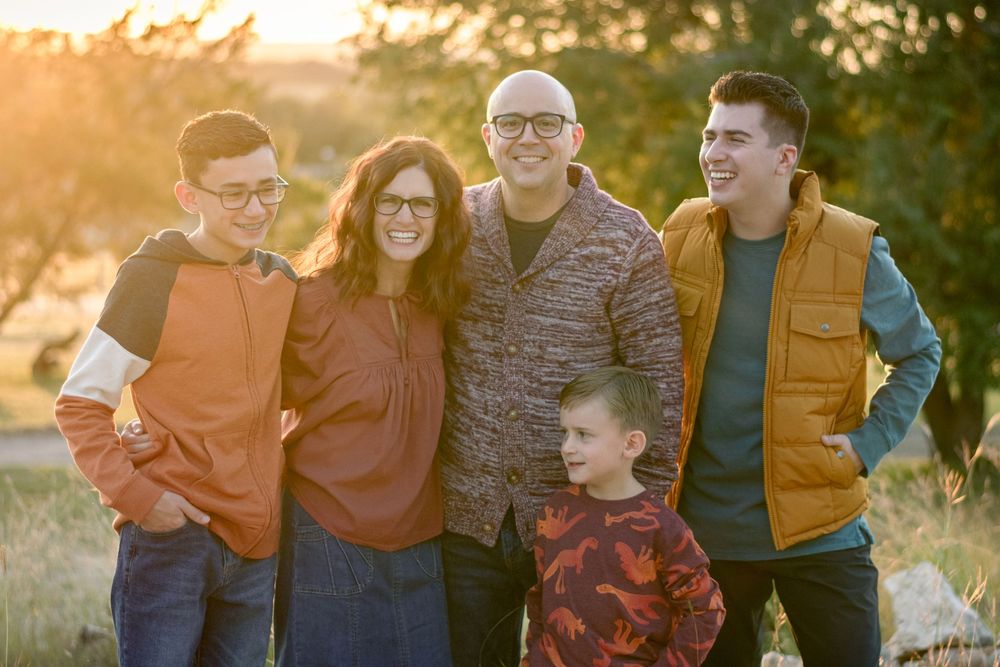 Family of five smiling outdoors at golden hour with warm sunset light in a natural setting.