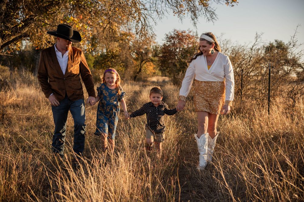 People walk through tall golden grass at sunset in a rural setting.