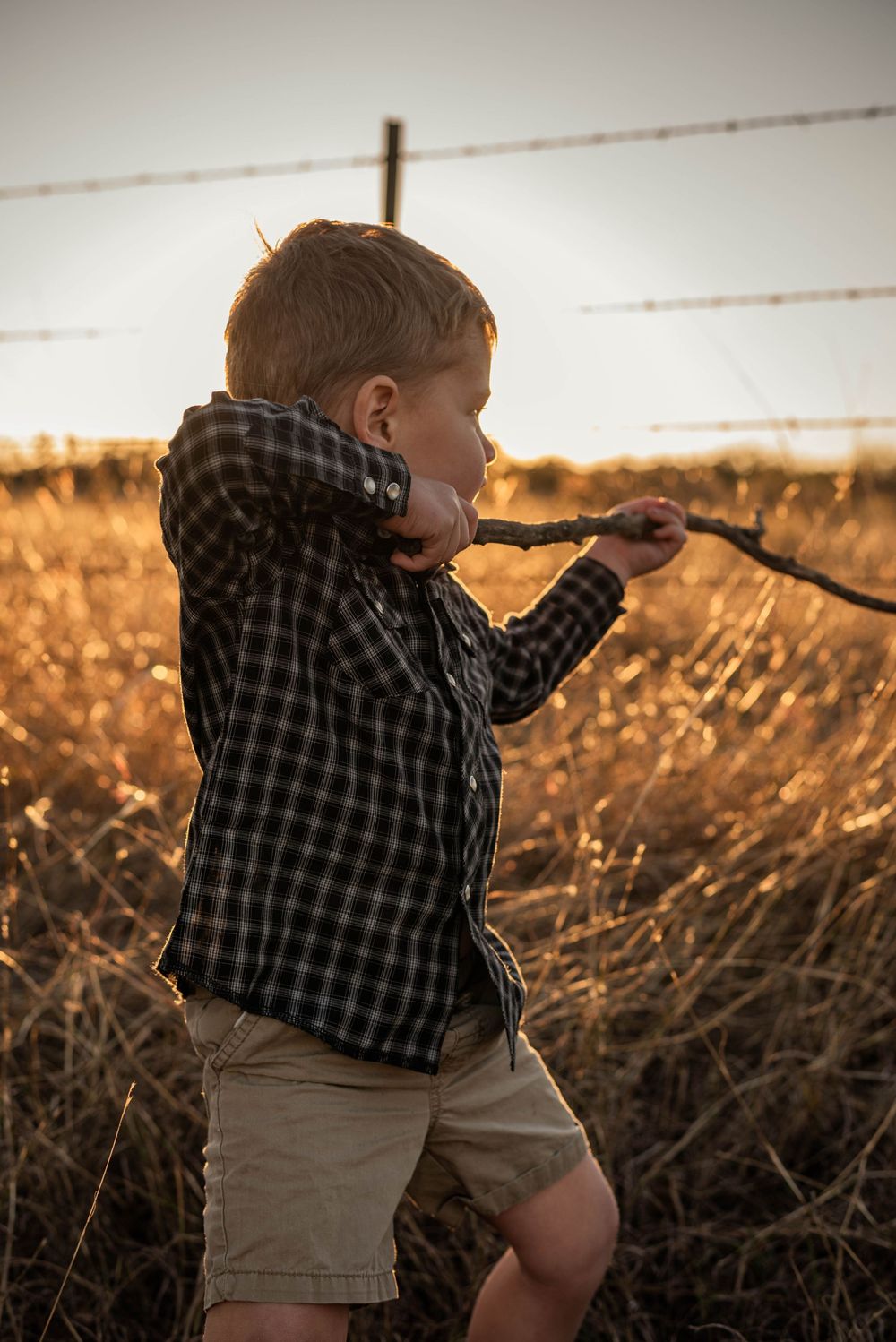 A small figure in plaid explores near a fence during sunset.