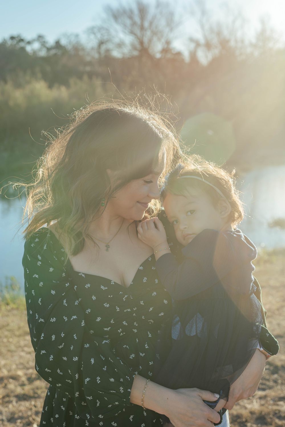 Two people embracing in sunlit field wearing dark patterned clothing.