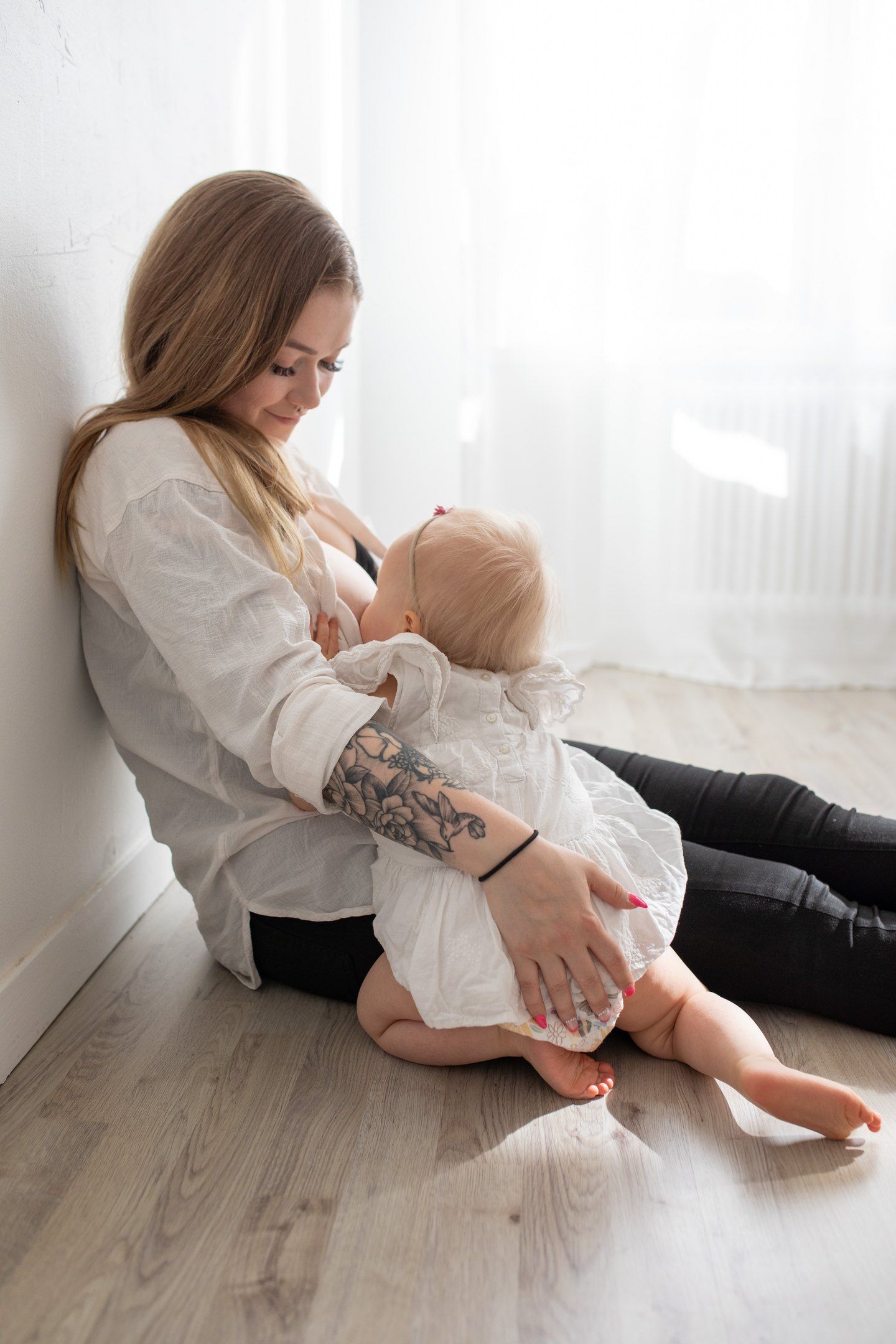 Imetyshetki. Äiti ja 1-vuotias tyttölapsi istuu studion lattialla, maitohetki taltioituna muistoksi. Imetyskuvaus, amningsfotografering.
