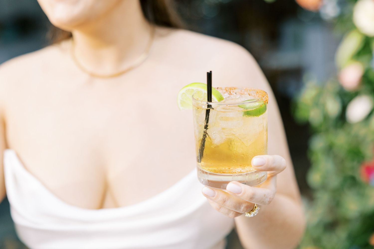 Woman holding a refreshing citrus cocktail garnished with lime in an outdoor garden setting.