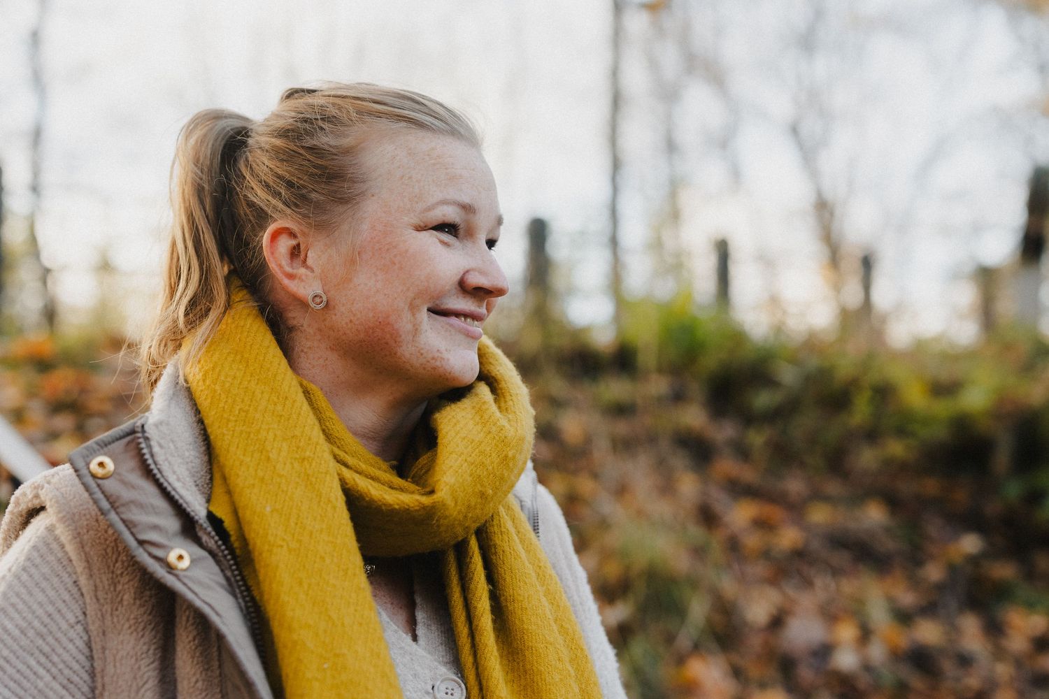 Syksyinen kuva hymyilevästä valokuvaajasta Annina Nygård. Okrankeltainen kaulaliina. Kuvan on ottanut Valokuvaaja Pinja Waris.
