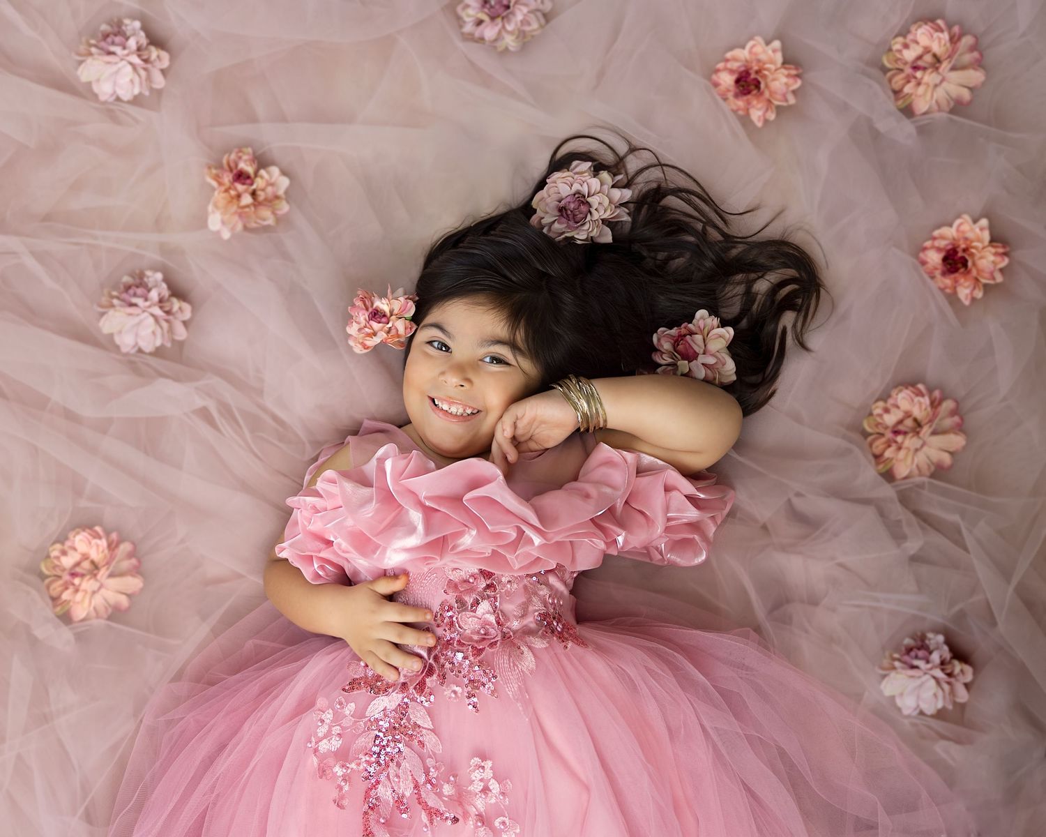 Overhead portrait on pink tulle fabric with scattered flower petals.