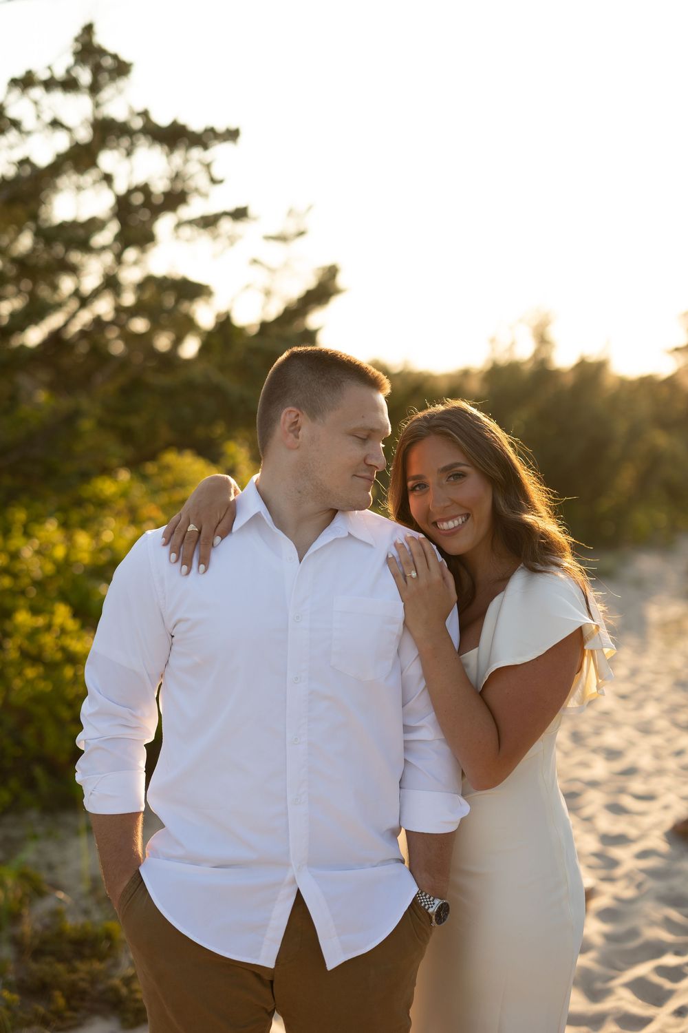 A couple shares a romantic moment on a sandy beach at sunset with warm golden lighting.