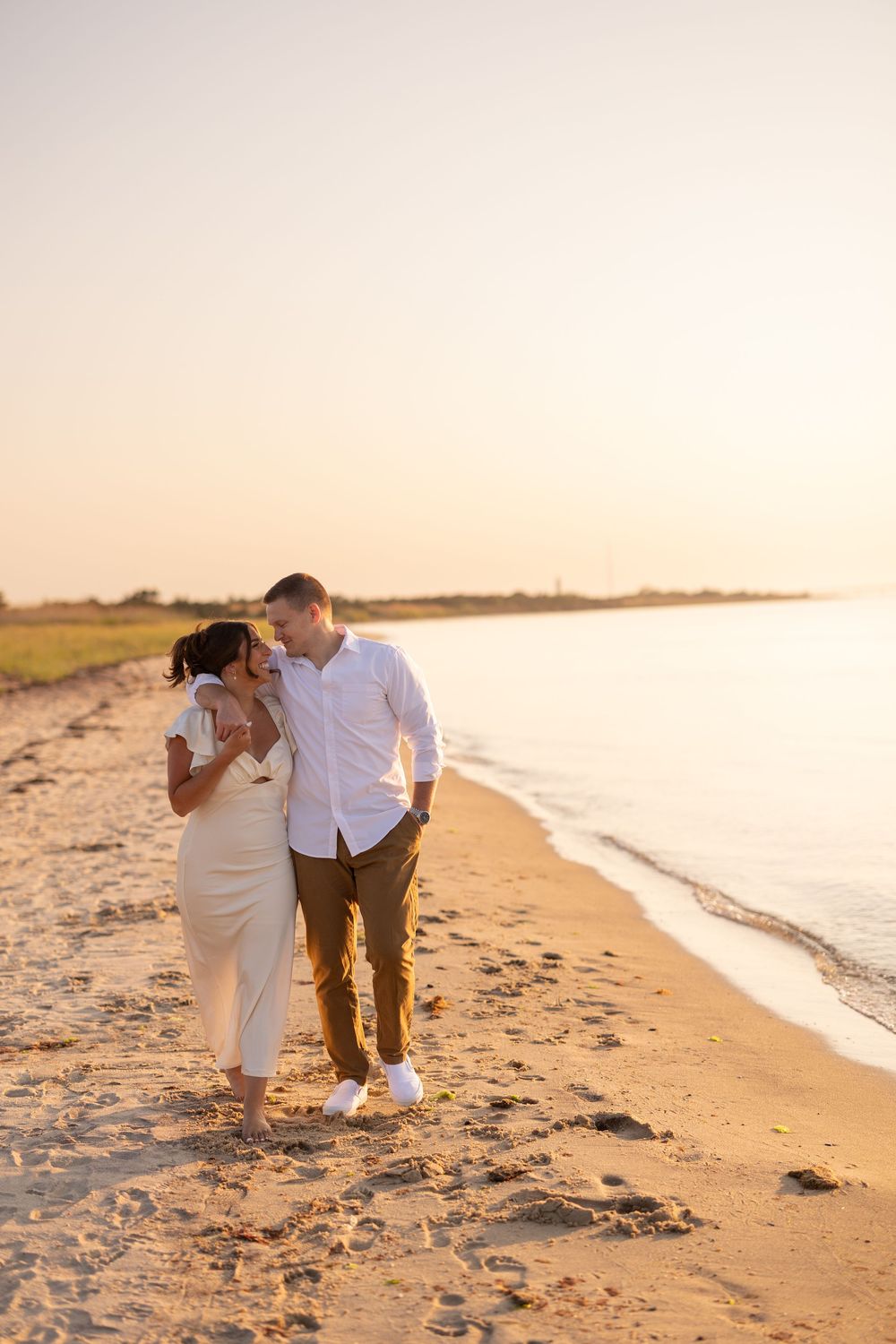 A couple walks intimately along a sandy beach at sunset with golden light illuminating their path.