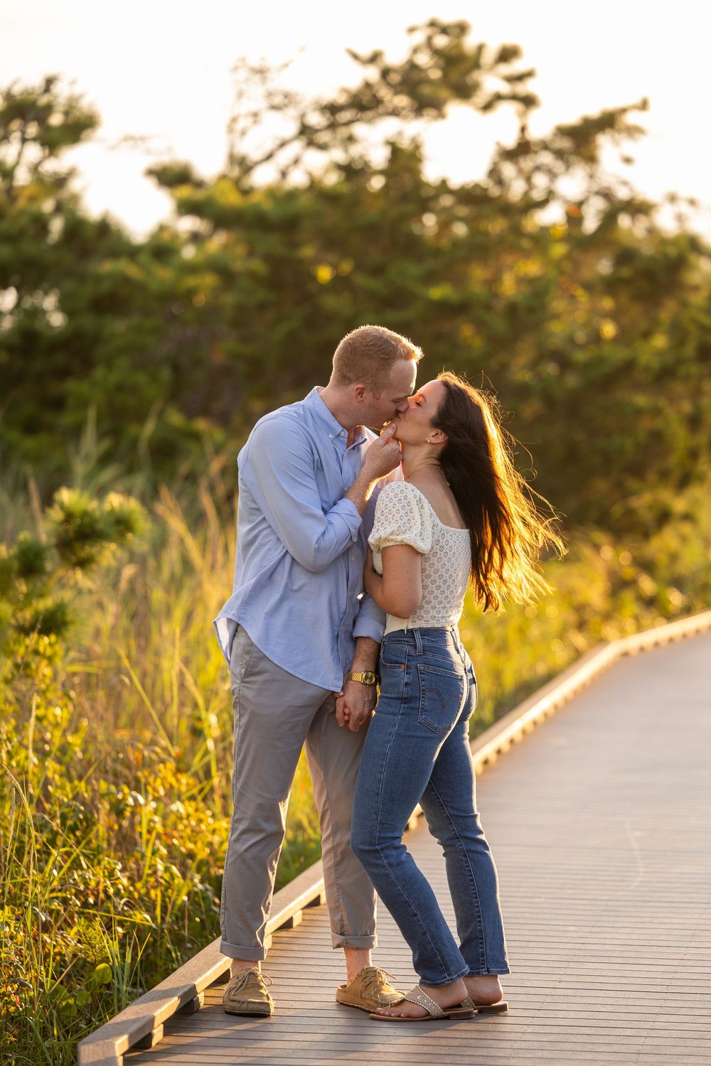 A couple shares intimate moments together on a wooden boardwalk during golden hour sunset.