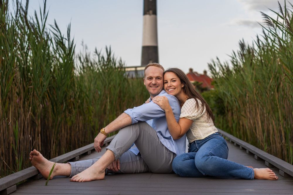 Couple lounging on wooden boardwalk surrounded by tall green reeds during daytime photoshoot.