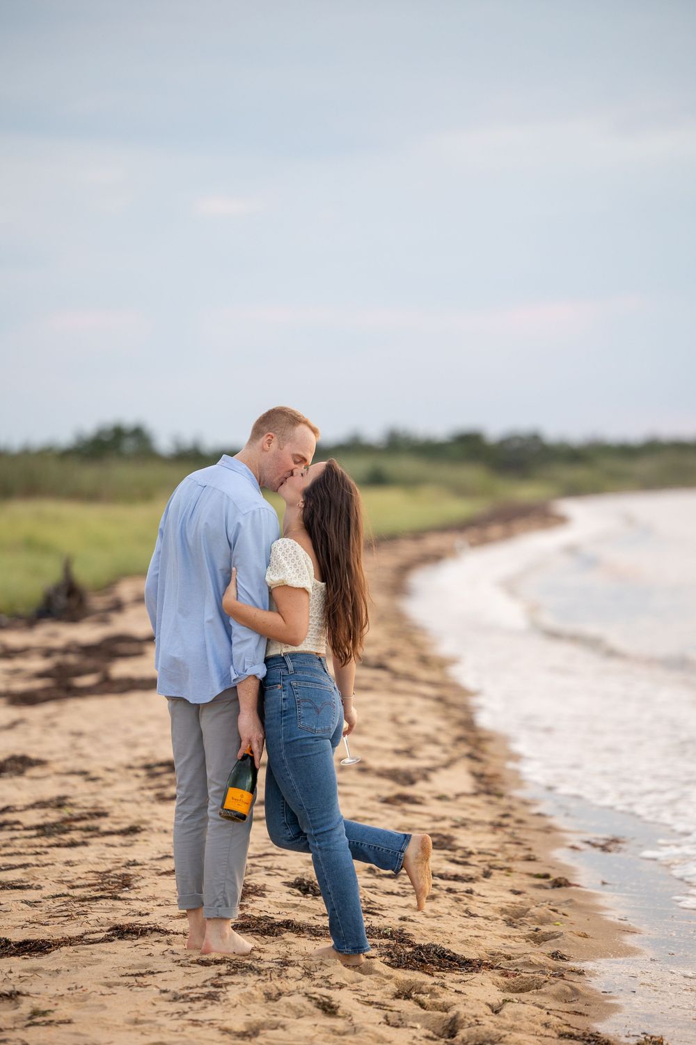 A romantic couple shares intimate moments together while walking along a sandy beach shoreline at sunset.