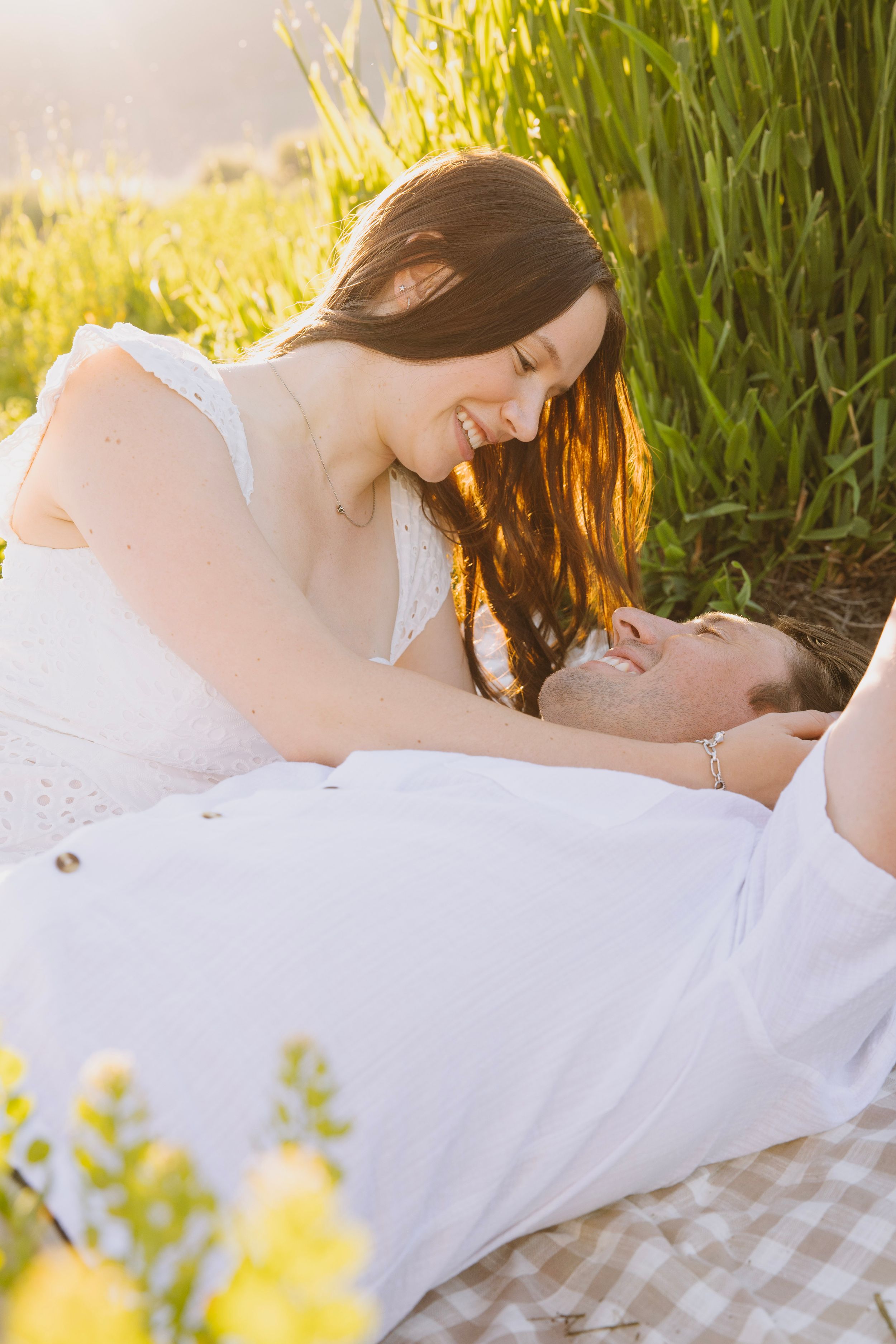 Romantic summer picnic scene with a couple in white clothing laying on a blanket surrounded by tall grass at golden hour.