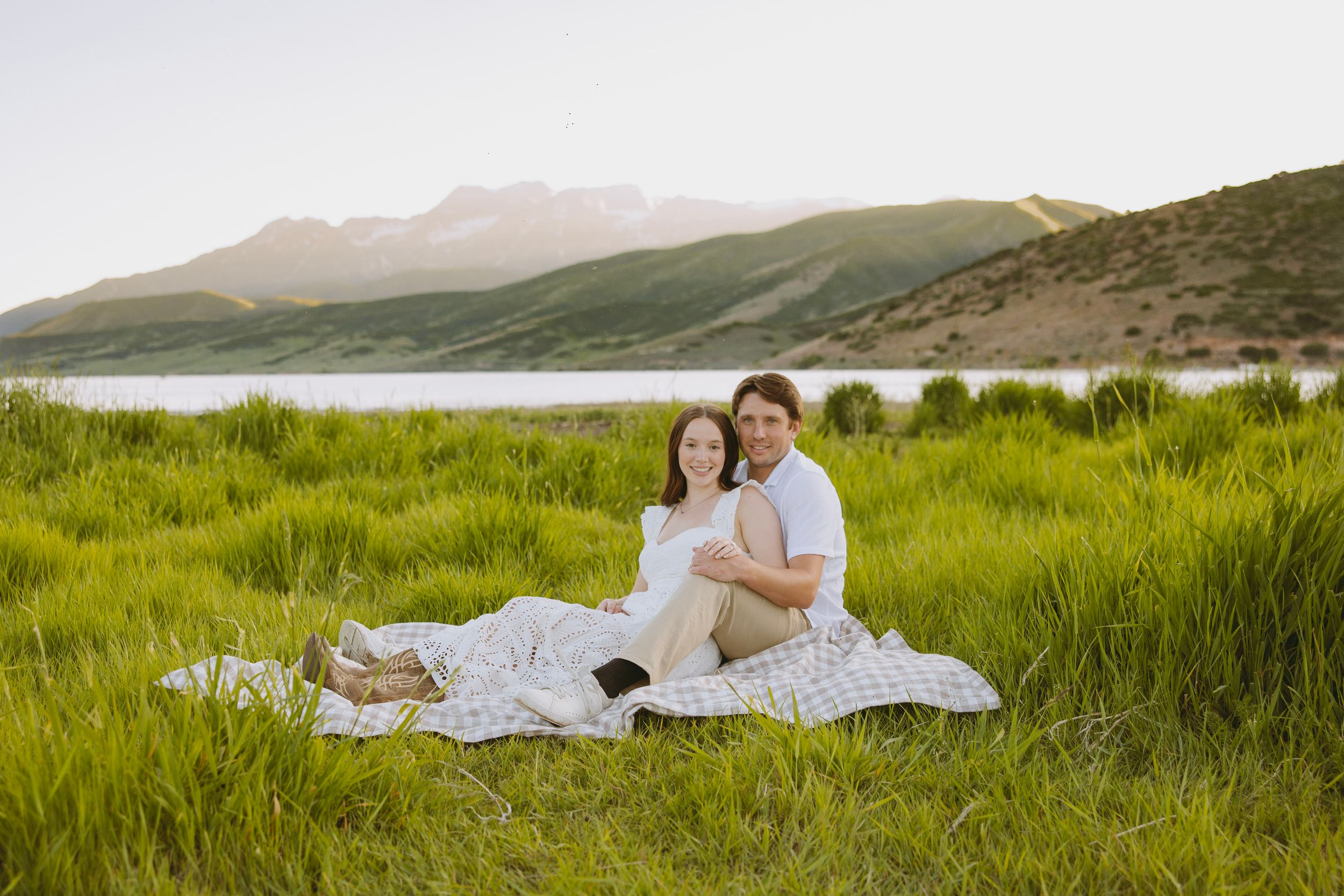 Rolling green hills and meadows stretch toward distant mountains beside a tranquil lake.