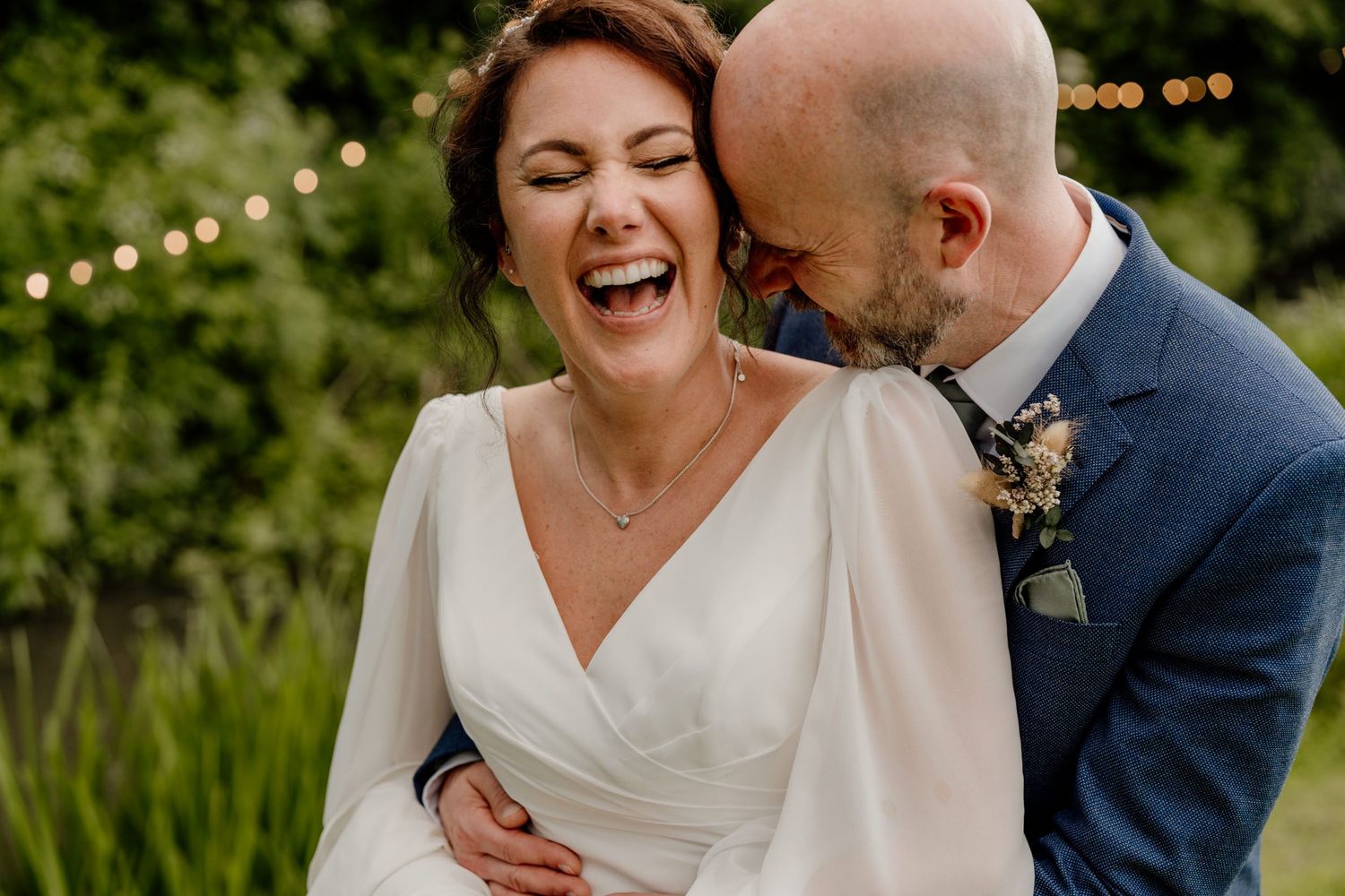 A joyful wedding couple sharing a candid laughing moment in an outdoor garden setting.