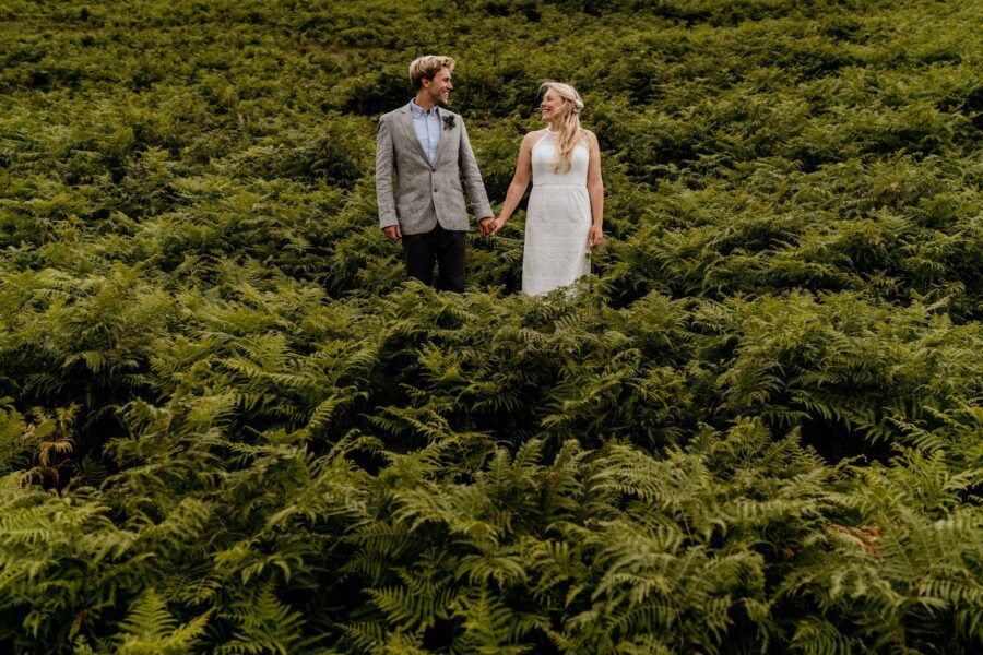 Couple walking through green garden pathway during wedding photoshoot.