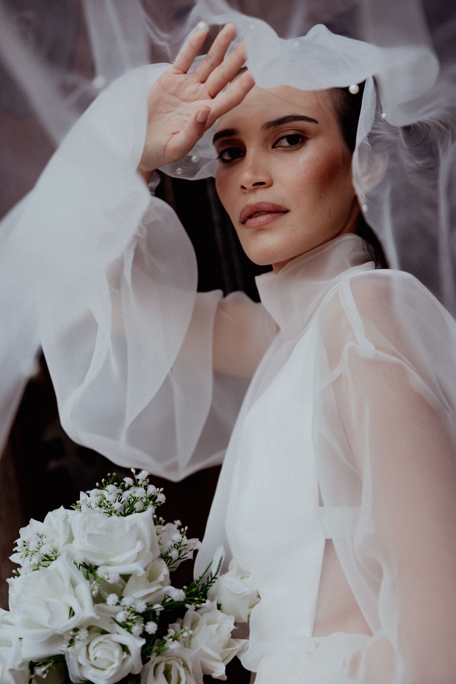 Bride in ethereal white veil holding classic white rose and baby's breath bouquet in romantic bridal portrait.