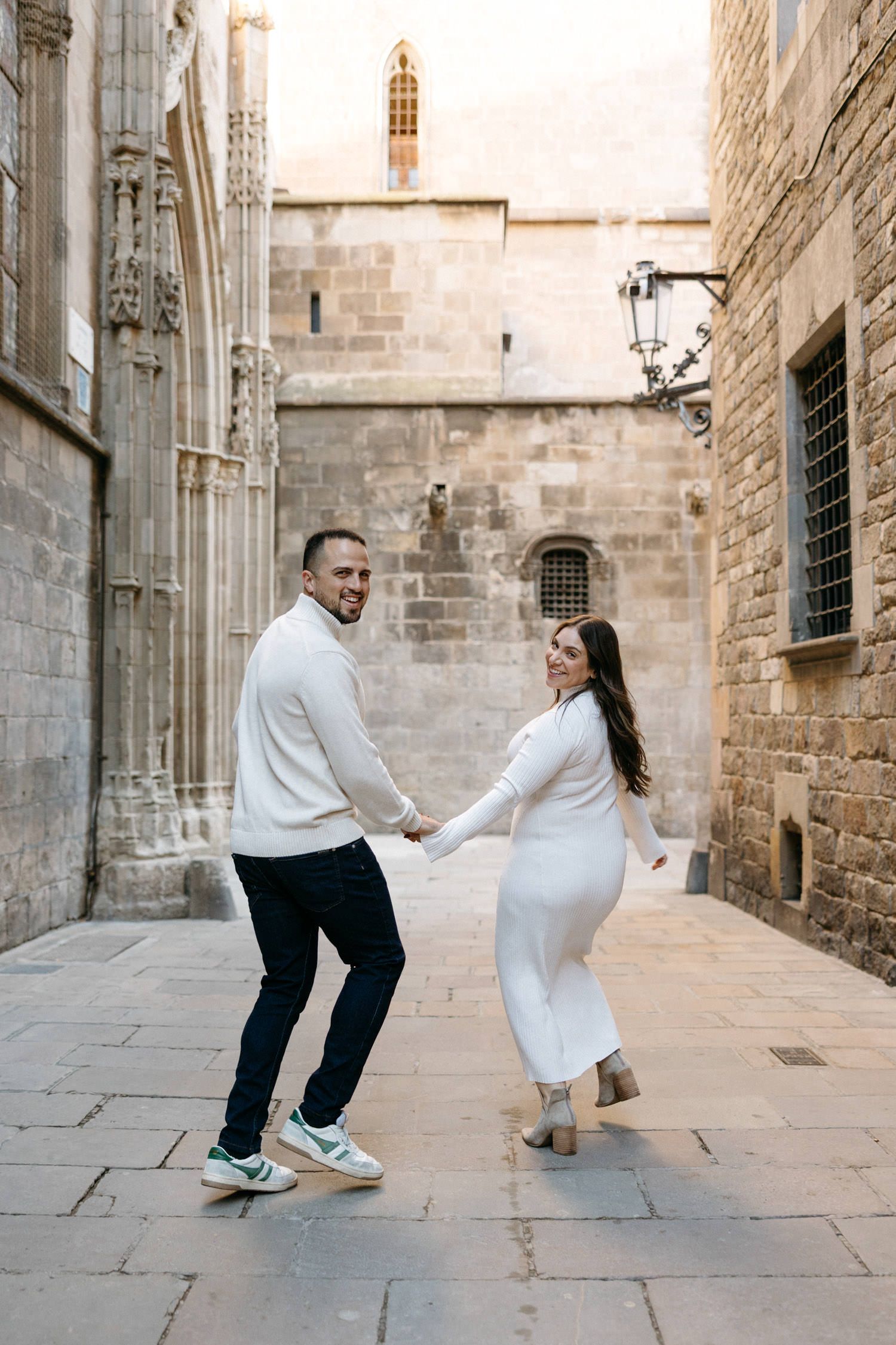 Couple dancing playfully on cobblestone street in front of historic stone building.