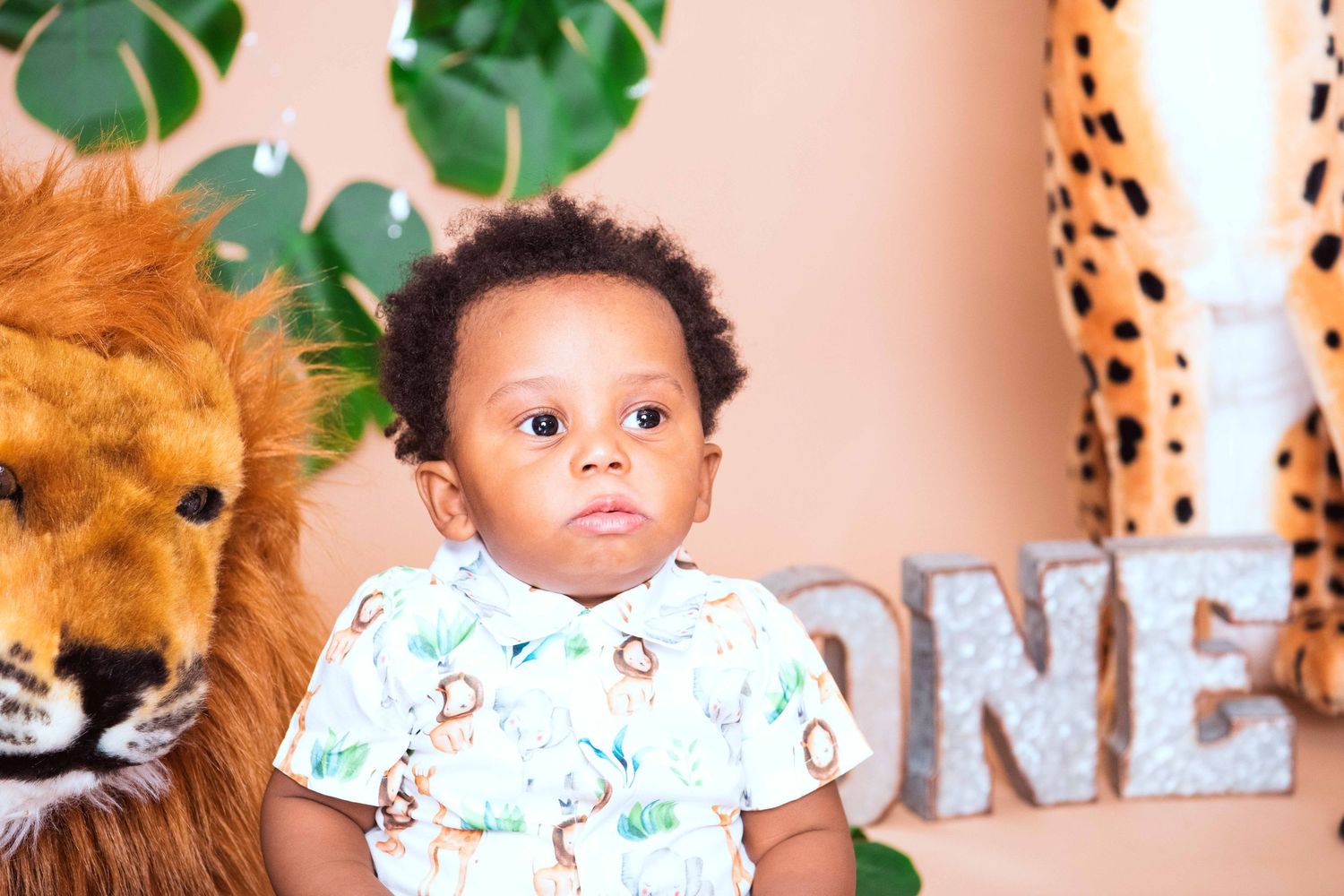 Safari themed birthday celebration with stuffed lion and decorative greenery against a peachy pink background.