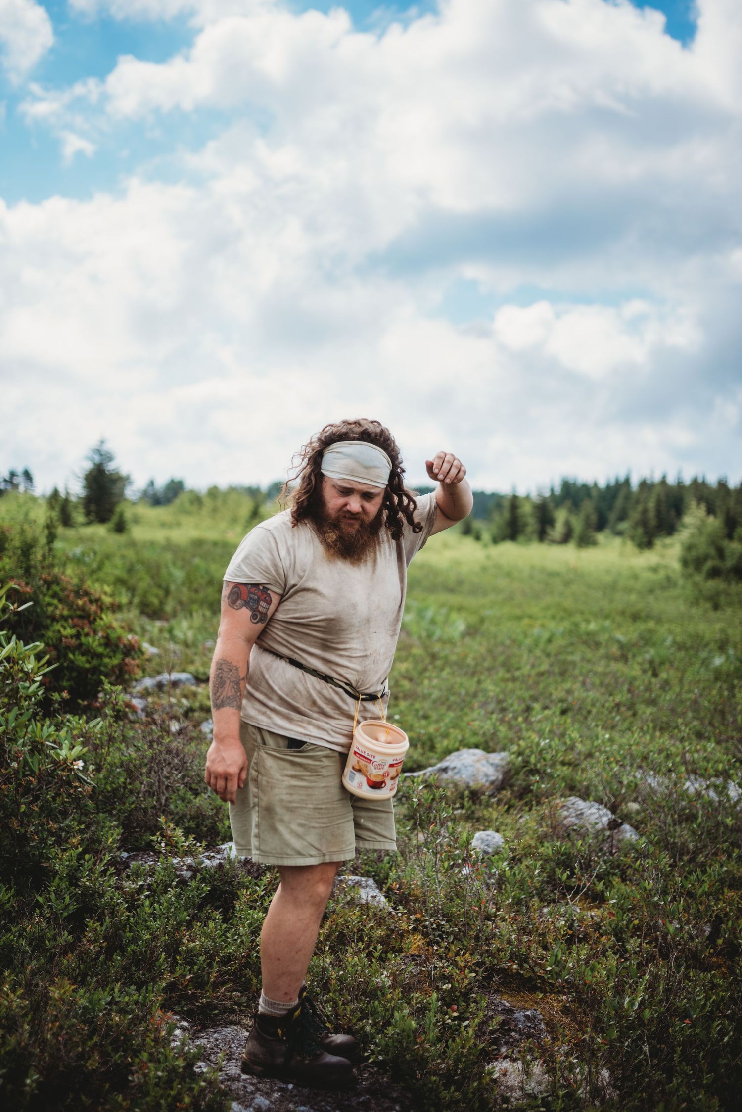 A hiker with a jar stands among wild vegetation on a sunny mountain landscape in Dolly Sods, WV.