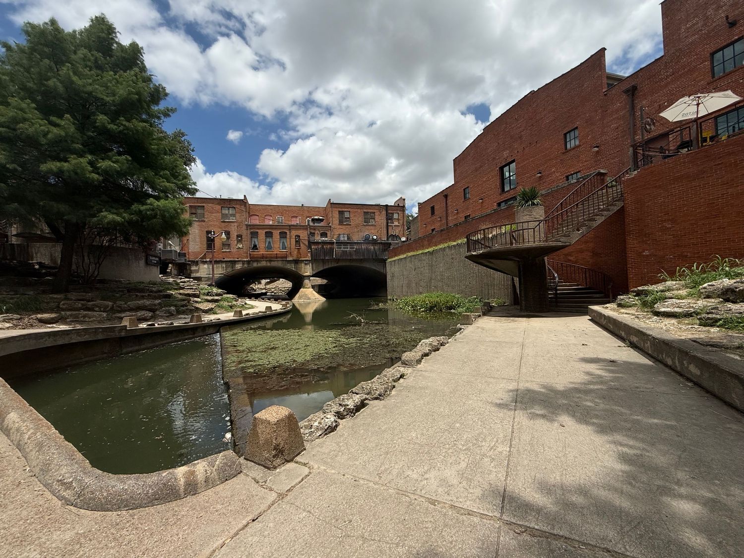 Panoramic view of an industrial brick building along a curved canal with stone walls and concrete walkways. fort worth stockyards