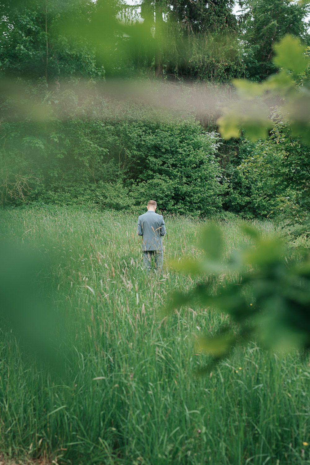 Figure stands in tall green grass field surrounded by lush foliage and trees on a dreamy summer day.
